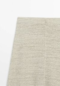 Gros plan d'un tissu tricoté gris clair avec une couture visible au centre sur un fond blanc.