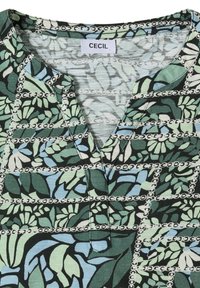Blouse à motifs de feuilles vertes, bleues et blanches avec des motifs de chaînes, col en V, et une étiquette de la marque "CECIL" à l'intérieur du col.