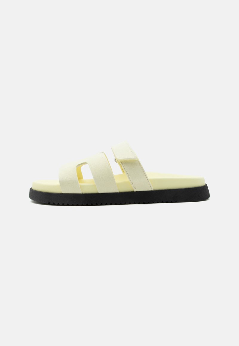 Sandale slide jaune clair avec trois brides et semelle noire rainurée, montrée de profil sur fond blanc.