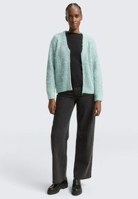 Licht teal gebreide cardigan met een textuurpatroon, open voorkant en geribbelde manchetten, gecombineerd met zwarte broeken en stevige zwarte schoenen.