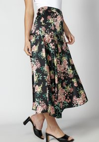 Musta kukkakuvioinen hame, jossa on korkea joustava vyötärö, polven pituinen leikkaus ja laskeutuva siluetti vaaleanpunaisilla ja vihreillä kukkakuoseilla.