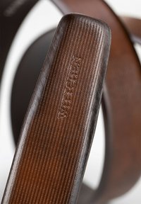Hnědý kožený pásek sandálu s texturovaným povrchem, obsahující vertikální linky a embosované logo pro detail. Zakřivený tvar, minimalistický design.