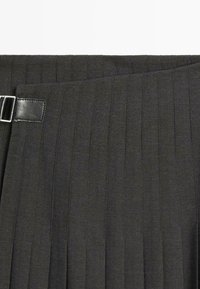 Sort plisseret nederdel lavet af tekstureret stof med en læderspænde ved taljen, der fremhæver lodrette striber i materialet.