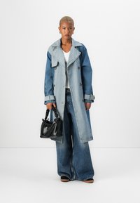 Denim trench coat with a wide collar, blue gradient, double-breasted design, and large pockets. Paired with loose blue jeans and a black handbag.