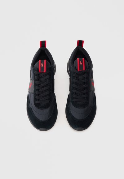 Μαύρα αθλητικά παπούτσια με κόκκινες λεπτομέρειες, μαύρα κορδόνια και κόκκινο λογότυπο αλόγου στη γλώσσα και την πλευρά, τοποθετημένα δίπλα δίπλα σε λευκό φόντο.