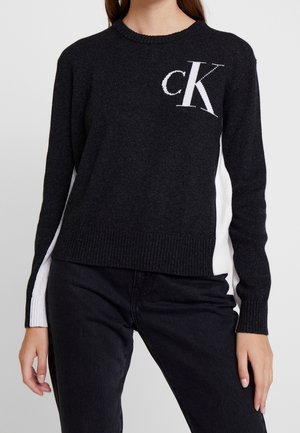 Pull noir avec des panneaux latéraux blancs et un logo "CK" blanc sur la poitrine. Encolure et poignets côtelés, fabriqué en matériau tricoté doux.