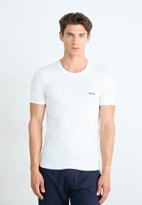 T-shirt blanc à manches courtes en coton, avec un col rond et un petit logo "BOSS" vert sur la poitrine gauche.