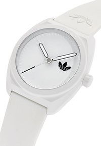 Fehér szilikon óra kerek arccal, ezüst részletekkel, fekete órajelzőkkel és három fekete és ezüst mutatóval; látható az Adidas logo.