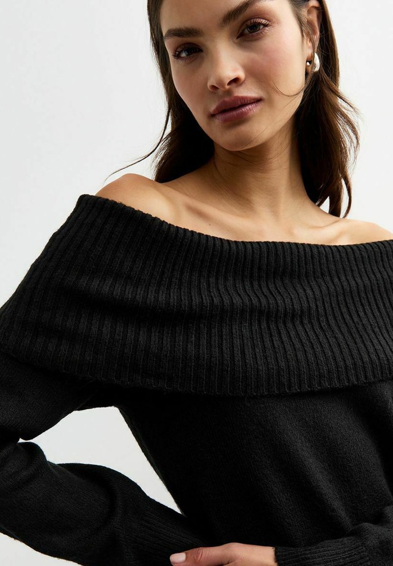 Maglione nero off-the-shoulder con scollo a costine e maniche lunghe. Tessuto morbido, vestibilità comoda e dettagli minimi.