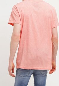 Różowa bawełniana koszulka z krótkim rękawem, lekko fakturowany materiał i luźny krój. Widok z tyłu z okrągłym dekoltem, bez ozdób.