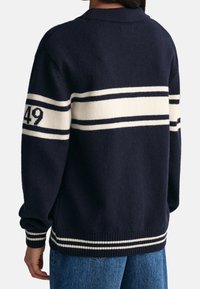 Granatowy sweter z dzianiny z białymi i kremowymi paskami, z numerem "49" na lewym rękawie oraz ribbowanym dołem i mankietami.