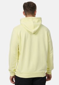Sudadera amarilla hecha de tela suave, con capucha regulable, puños acanalados y un corte relajado. La vista trasera muestra un diseño limpio y sencillo.