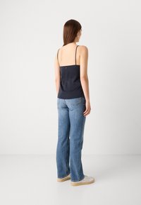 Mørkeblå satin cami med tynne stropper, en tettsittende design og en subtil knappedetalj bak. Brukt med lyseblå senejeans.