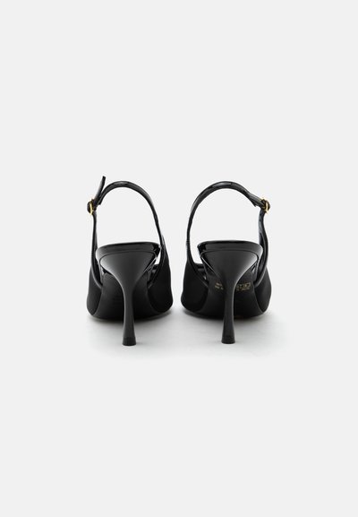 Chaussures slingback noires à talons aiguilles fins, vues de dos sur fond blanc.