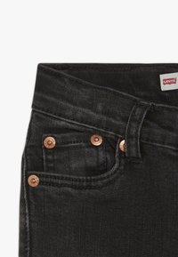 Vaqueros de denim negro de cintura alta, con herrajes de cobre, un pequeño bolsillo frontal y una etiqueta de Levi's visible. Textura suave.