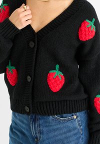 Pletený černý cardigan s vyvýšenými, texturovanými červenými jahodami se zelenými listy. Přední knoflíky a žebrované manžety a lem.