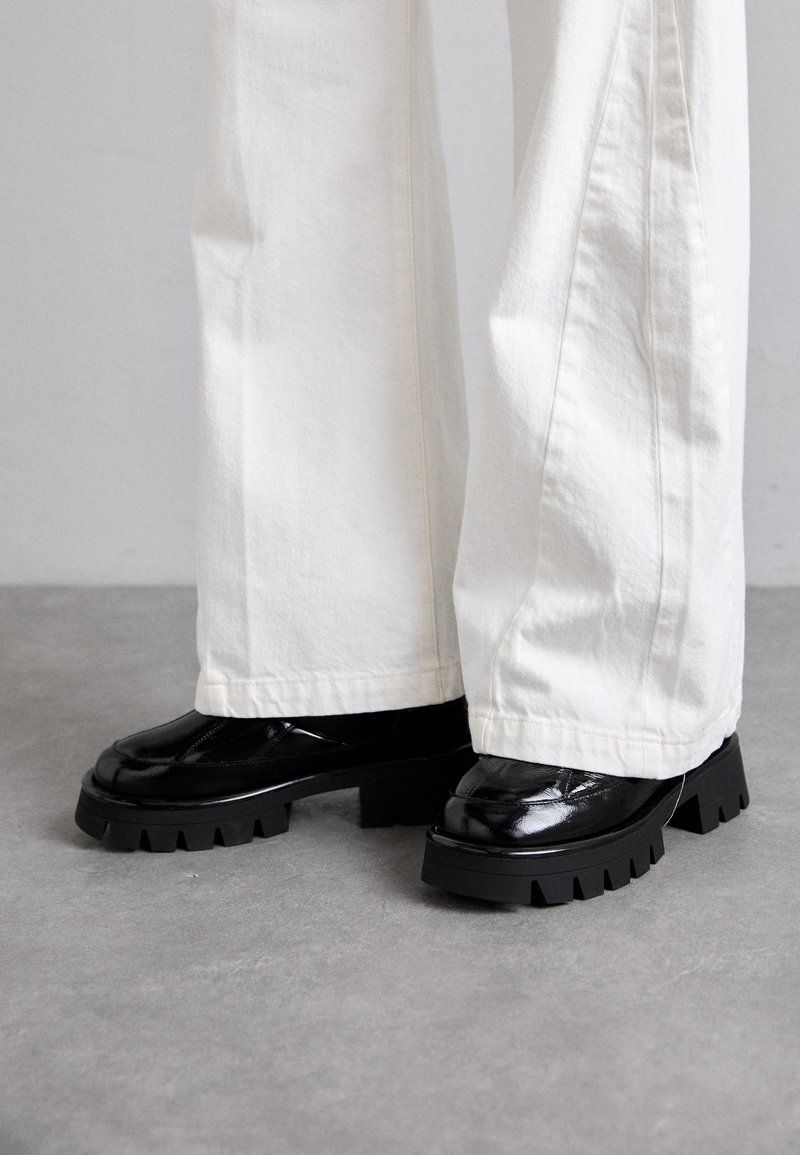 Black chunky-soled shoes with a glossy finish, paired with white wide-leg pants. Notable thick tread and smooth texture on shoes.