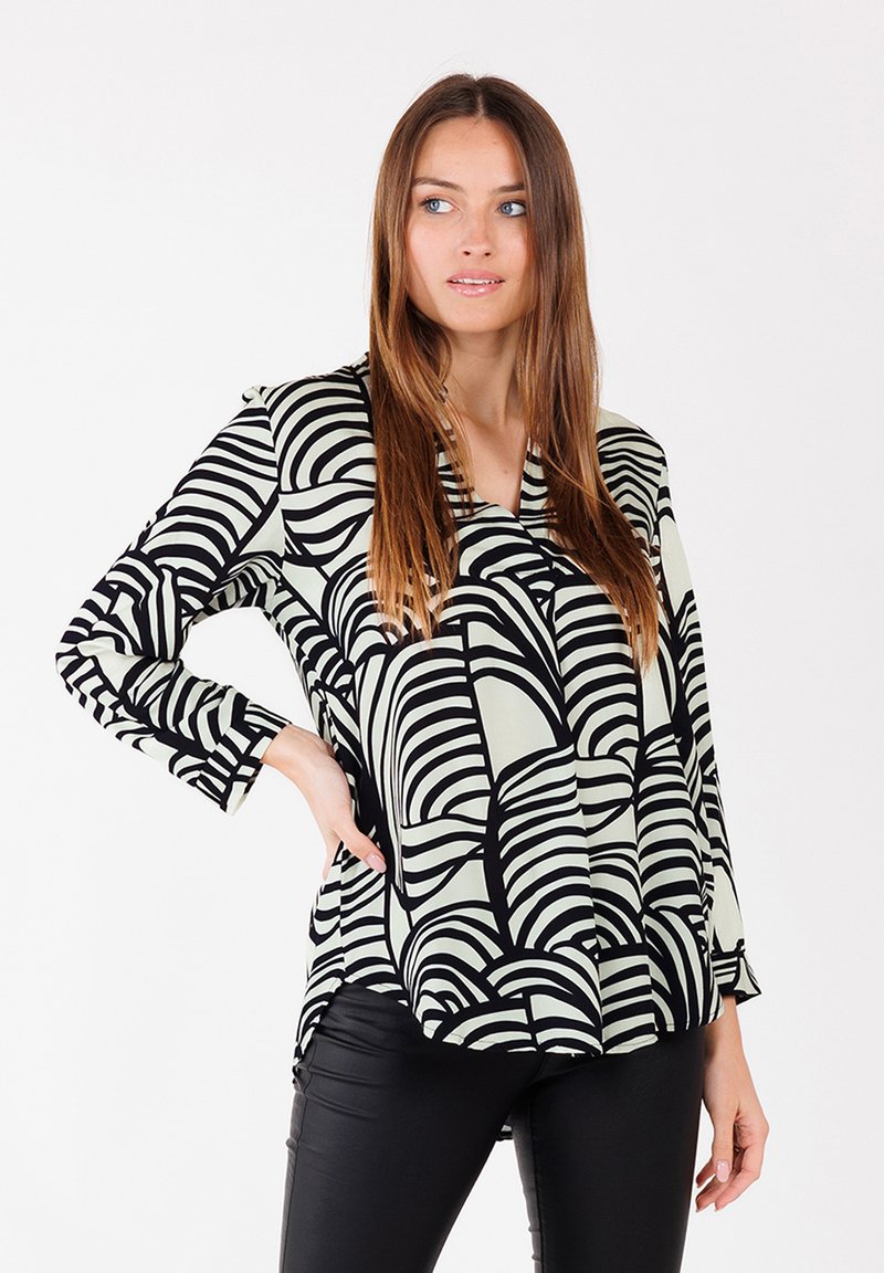 Zwart-wit gebladerde blouse met lange mouwen, met een abstract ontwerp op een lichtgroene achtergrond, gemaakt van een gladde stof.
