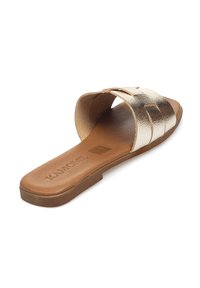 Sandalia plana de metal dorado con suela marrón y diseño abierto. La parte superior presenta una textura suave y brillante con simples acentos recortados.
