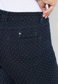 Tmavé džíny z denimu se jemným tečkovaným vzorem, elastickým pasem a dvěma malými zadními kapsami s kovovými knoflíky.