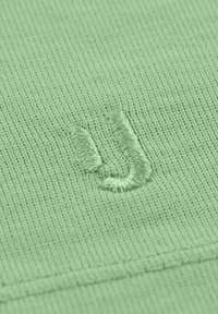 Jasnozielona dzianina z teksturową powierzchnią, z wyszytym literą "U" w pasującym kolorze. Prosty design, bez wzorów.