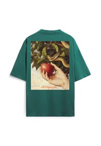 Turquoise T-shirt met een afbeelding op de achterkant van een hand die een rode appel vasthoudt naast een slang die zich om boomtakken krult, met de tekst "The Original Sin" eronder.