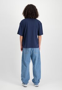 Marineblauw t-shirt met korte mouwen in een relaxte pasvorm, gecombineerd met lichtblauwe baggy jeans. De stof lijkt zacht en casual met minimale details.