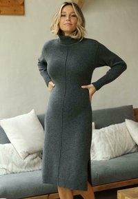 Robe en tricot gris avec col roulé, manches longues et fentes sur les côtés. Texture lisse et design ajusté, atteignant le milieu du mollet.