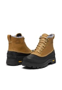 Bottes en cuir marron clair et caoutchouc noir avec doublure en polaire grise, tiges texturées, œillets en métal et semelle Vibram pour l'adhérence.