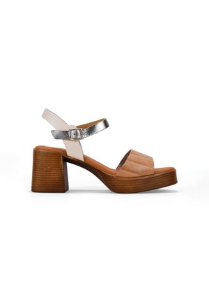 Sandalias de tacón abiertas en color marrón claro y crema, con una correa de tobillo plateada, tacón de bloque de madera y detalles texturizados en la parte superior.