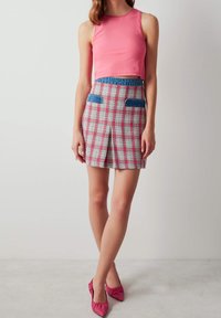 Top corto rosa combinado con una minifalda de cuadros que presenta bolsillos azules; completo con zapatos planos puntiagudos rosas. Texturas suaves y colores vibrantes.