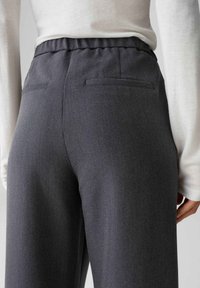 Grijze broek met een gestructureerde stof, voorzien van een hoge elastische taille, twee achterzakken en een relaxte pasvorm. De tailleband is geplooid.