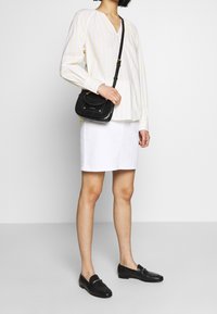 Bílá džínová sukně, dlouhý rukáv žluté a bílé proužkované tričko, černá přes rameno nositelná taška a černé mokasíny. Hladká látka a přizpůsobený střih.