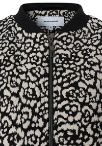 Schwarz-weiße Jacke mit Reißverschluss, die ein Leopardenmuster, einen gerippten schwarzen Kragen und eine Reißverschlussverzierung vorne aufweist. Markenschild innen sichtbar.