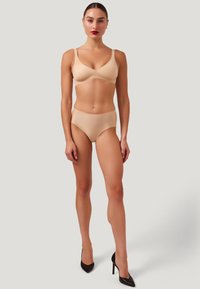 Nude lingerie-set bestående av en sömlös bh med justerbara band och matchande högmidjade trosor; slät textur och minimalistisk design.