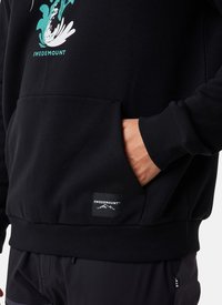 Sweatshirt en coton noir avec une poche avant, des poignets côtelés et un patch logo. Le design comprend un motif de vagues en teal et blanc.