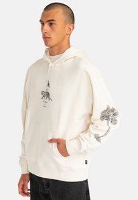 Cream hoodie made of soft fabric, featuring black animal and palm tree prints on front and sleeve, with a front pouch pocket and drawstring hood.