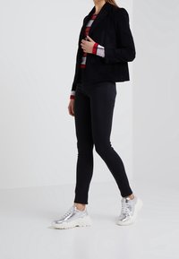 Blazer de pana negra, camiseta de manga larga a rayas rojas y blancas, jeans skinny negros y zapatillas metálicas plateadas con suelas gruesas blancas.
