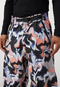 Αφαιρετικές παντελόνες με σχέδιο σε μαύρο, λευκό, ροζ και μπλε χρώμα; διαθέτουν ελαστική μέση με μαύρη ζώνη και τσέπες με φερμουάρ.