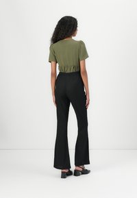 Haut vert olive avec des manches bouffantes et une taille froncée, associé à un pantalon noir évasé avec un motif texturé, porté avec des chaussures noires.
