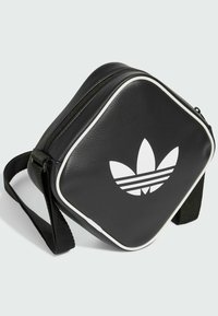 Černá syntetická crossbody taška čtvercového tvaru s bílým lemováním a velkým bílým logem Adidas trefoil na přední straně. Součástí je nastavitelný popruh.