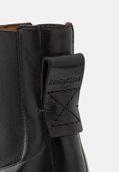 Botín negro de cuero con panel lateral elástico, detalles cosidos y una lengüeta de marca con acentos de pespunte.