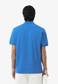 Kortärmad polo i ljusblå bomull, med klassisk krage och enkel design, med rak nederkant och sidofickor.