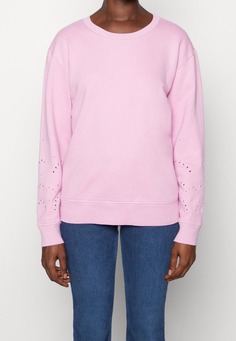 Sudadera rosa con cuello redondo, mangas largas y patrones de ojales decorativos en las mangas. Material suave, corte relajado.