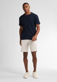 Námořnické tričko s krátkým rukávem a kontrastním výstřihem, kombinované se světle béžovými šortkami. Model má na sobě krémové tenisky. Jednoduchý design, volný střih.