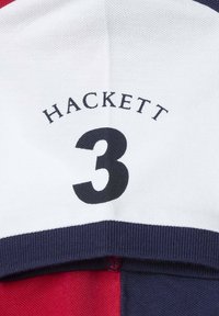 Polo shirt aux couleurs rouge, blanc et bleu marine. Logo "HACKETT" et le chiffre "3" affichés en évidence sur la poitrine. Tissu texturé.