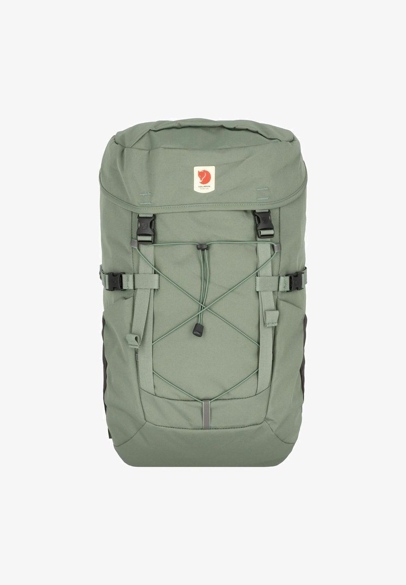 Zelený látkový batoh s rolovacím designem, nastavitelné popruhy, přední bungee šňůra, boční přezky a nášivka s logem na přední straně.