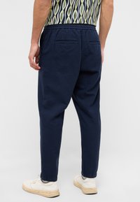 Granatowe spodnie casualowe z elastycznym paskiem, z dwoma tylnymi kieszeniami i zwężanymi nogawkami, połączone z białymi trampkami.