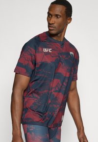 Ανδρικό αθλητικό κοντομάνικο μπλουζάκι σε ναυτικό μπλε και μαρόν με αφηρημένο σχέδιο. Διαθέτει λογότυπο UFC στο στήθος. Ομαλό, ελαφρύ ύφασμα.