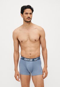 Moške modre bokserice z teksturiranim temno modrim pasom, ki ima bel Nike logotip. Gladko blago in prilegajoč dizajn.